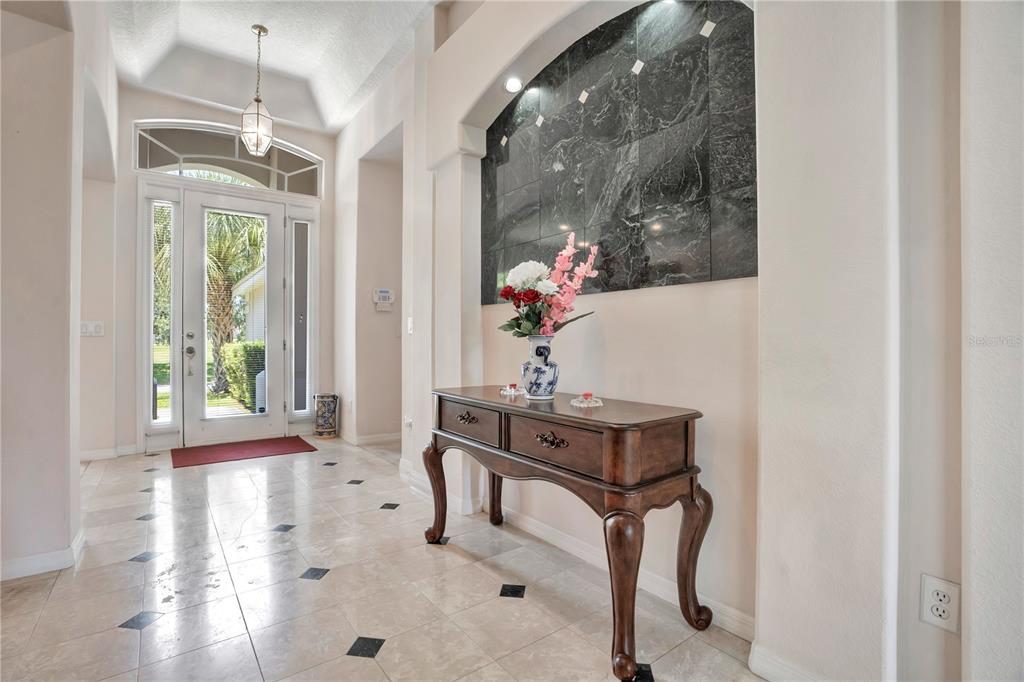 A foyer features a tile floor with black accents, a dark wood console table, and marble — 1709 GOLFVIEW DRIVE, KISSIMMEE, FL