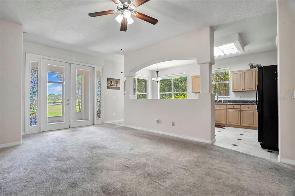 A living room with gray carpet, a ceiling fan, and an arched opening to a kitchen — 1709 GOLFVIEW DRIVE, KISSIMMEE, FL