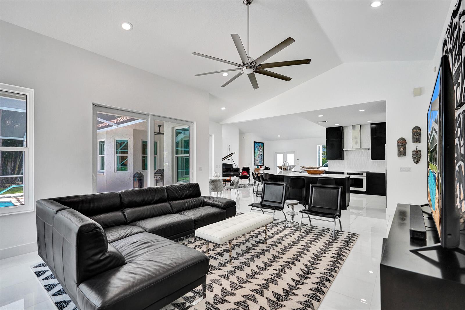A modern open-concept living room features a black sectional sofa, white tile floors, and kitchen — 4300 Hunting Trail, Lake Worth FL 33467, LAKE WORTH, FL
