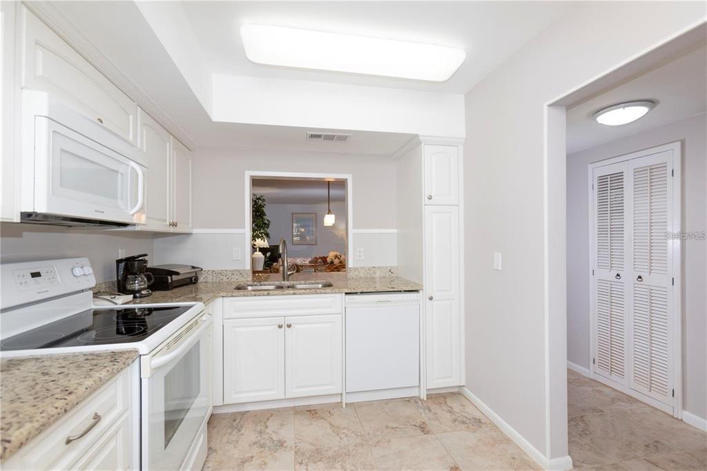 A kitchen features white cabinetry, granite countertops, a white stove, and a pass-through window — 4632 MARINE PARKWAY UNIT 201, NEW PORT RICHEY, FL