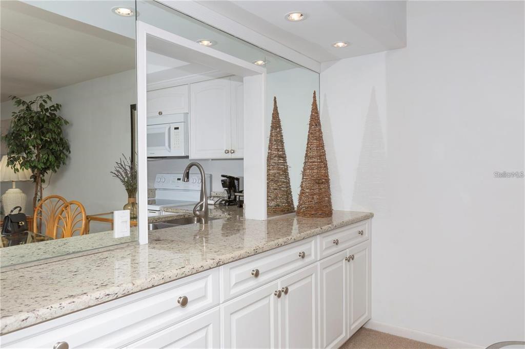 A kitchen pass-through window with a granite countertop and white cabinets overlooks a dining area — 4632 MARINE PARKWAY UNIT 201, NEW PORT RICHEY, FL