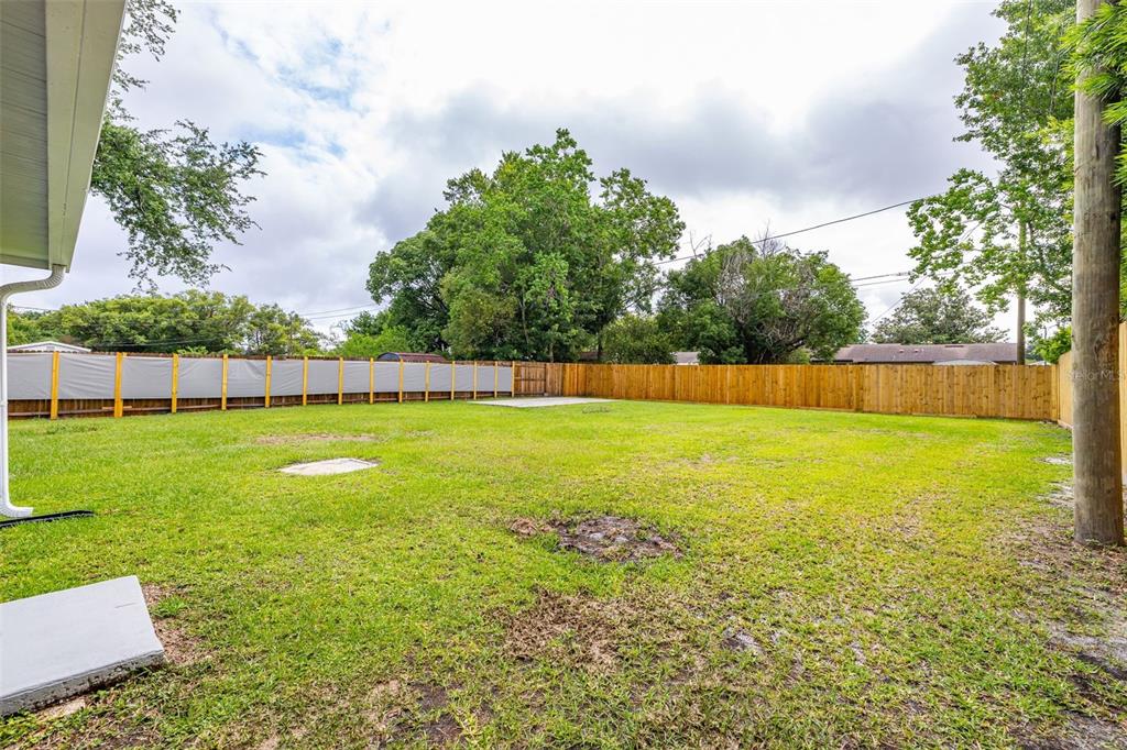 A fenced backyard features a grassy lawn, a concrete patio, and mature trees — 235 TENNESSEE AVENUE, ST CLOUD, FL