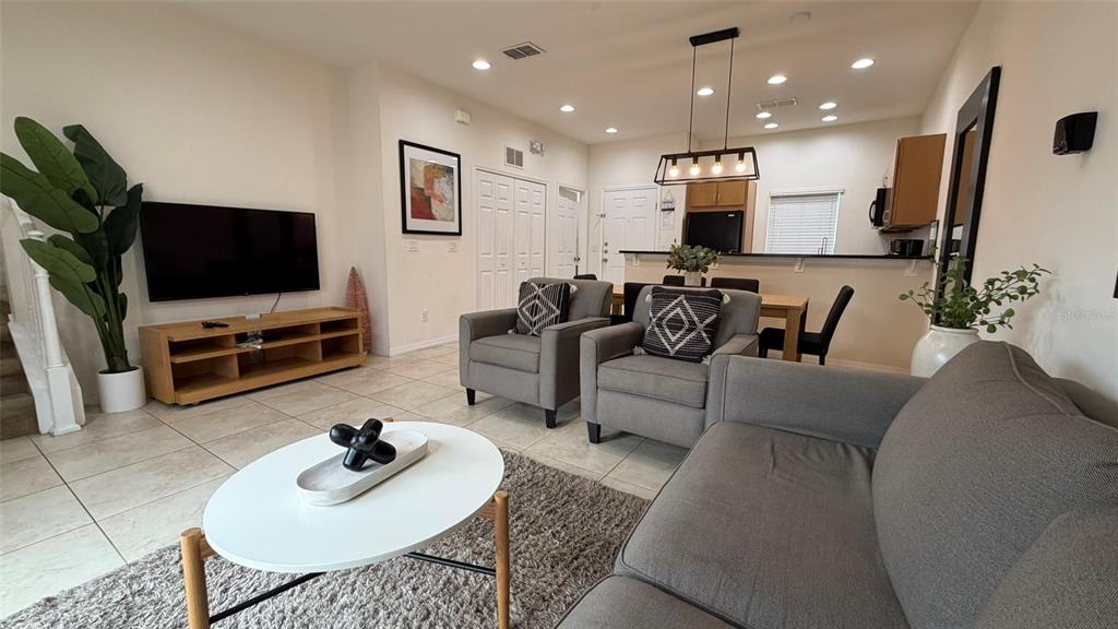 A living room with tile flooring, a grey sofa, two armchairs, and an open kitchen — 3021 RED GINGER ROAD, KISSIMMEE, FL