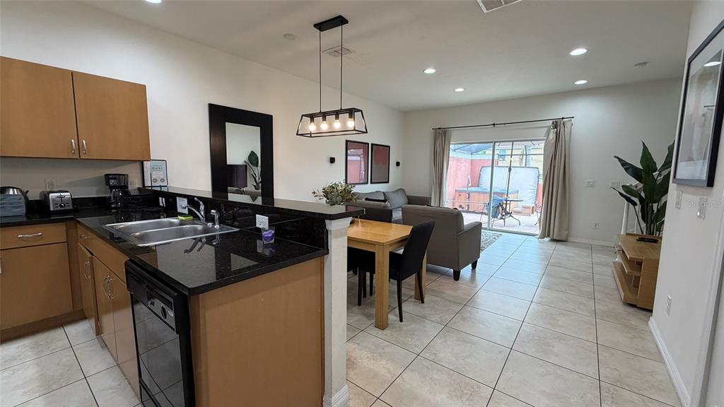 A kitchen with dark countertops overlooks a dining area and living room with patio access — 3021 RED GINGER ROAD, KISSIMMEE, FL