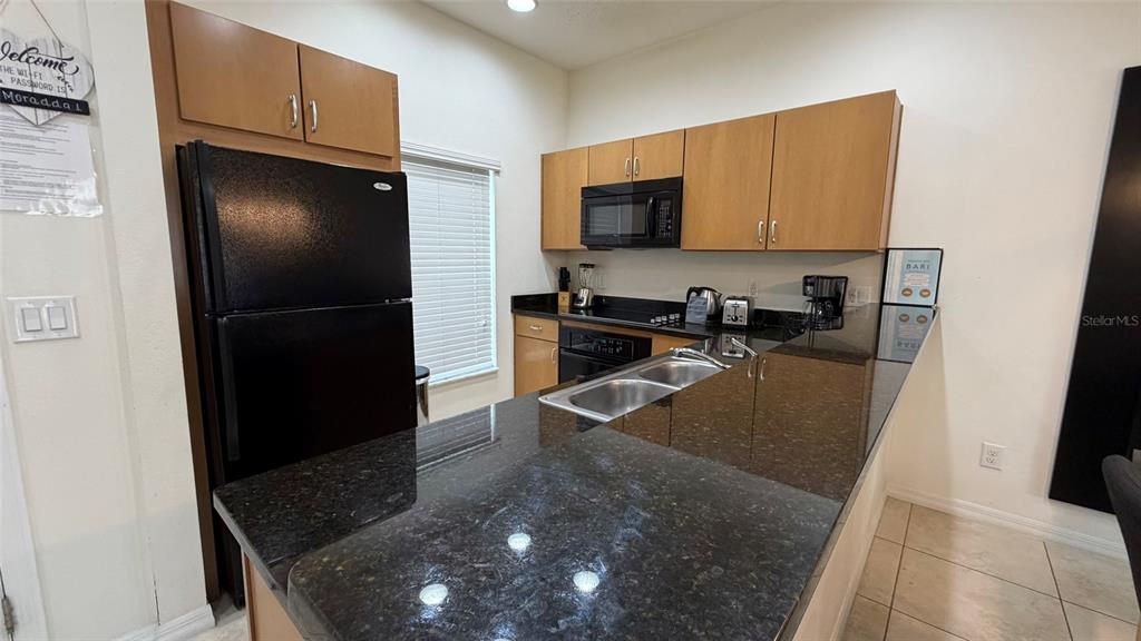 A kitchen features dark granite countertops, light wood cabinets, and black appliances — 3021 RED GINGER ROAD, KISSIMMEE, FL
