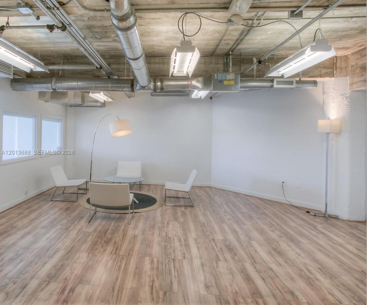 An open-concept room features exposed industrial ductwork, concrete ceilings, and light wood-look flooring — 605 Lincoln Rd # 460, Miami Beach FL 33139, MIAMI BEACH, FL