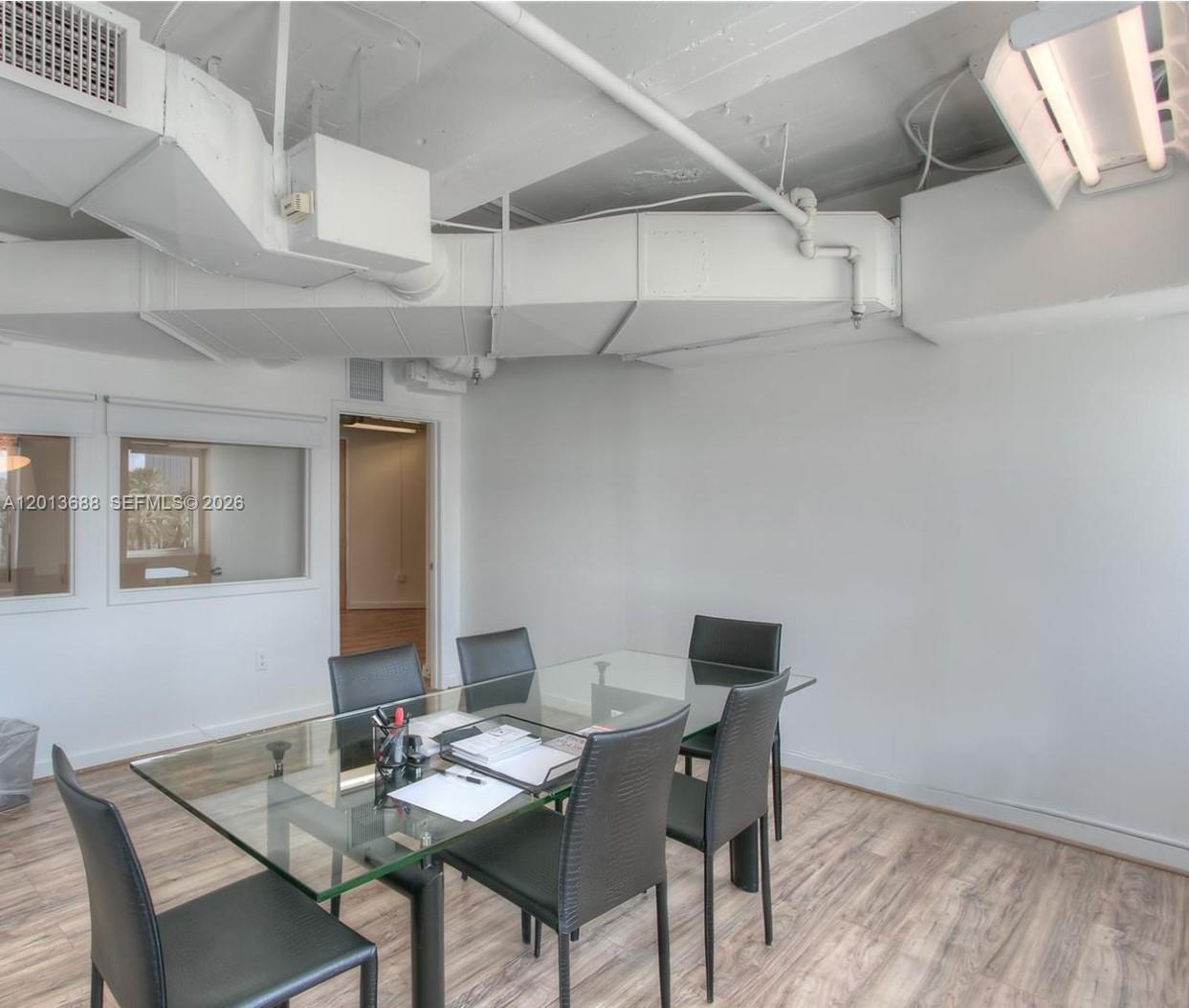 A conference room features a glass table, black chairs, wood-look flooring, and exposed white ductwork — 605 Lincoln Rd # 460, Miami Beach FL 33139, MIAMI BEACH, FL