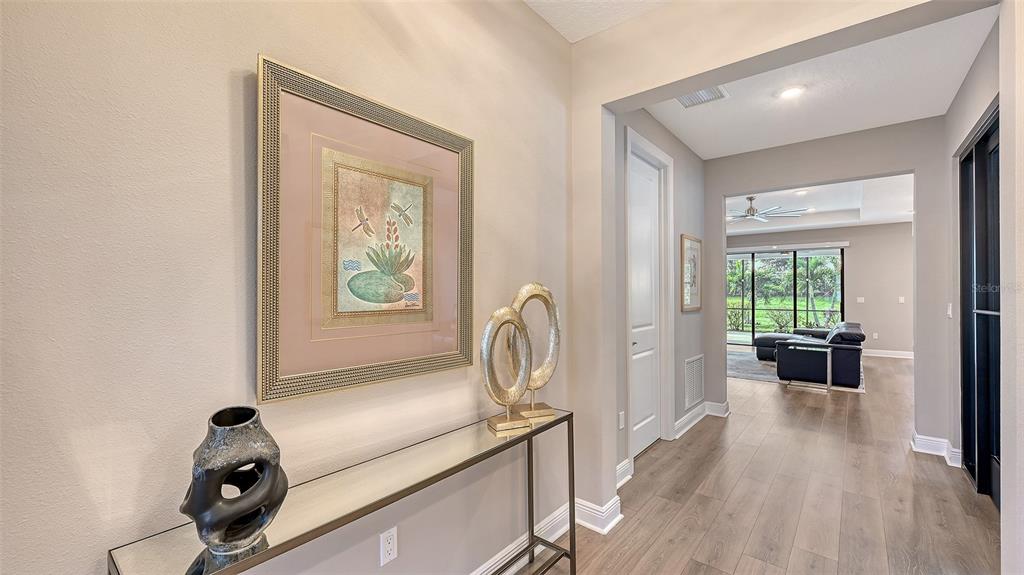 A hallway with wood-look flooring leads to a living area with a view of the outdoors — 17202 CRESSWIND TERRACE, BRADENTON, FL