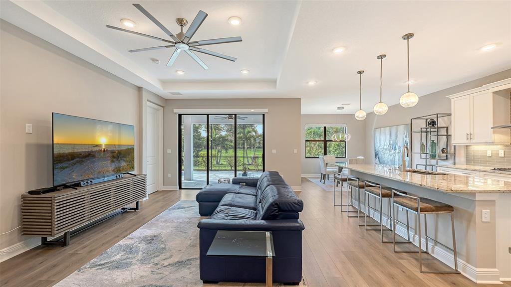An open-concept living room and kitchen featuring a blue sofa, large television, and island seating — 17202 CRESSWIND TERRACE, BRADENTON, FL