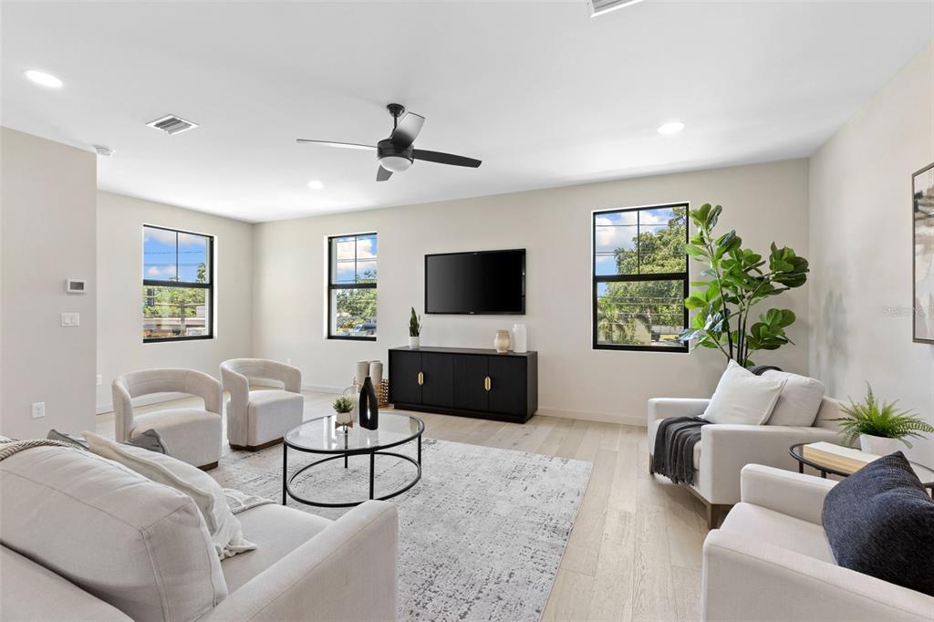 A bright living room features light wood floors, neutral furniture, a black media console, and windows — 2211 16TH STREET N, ST PETERSBURG, FL
