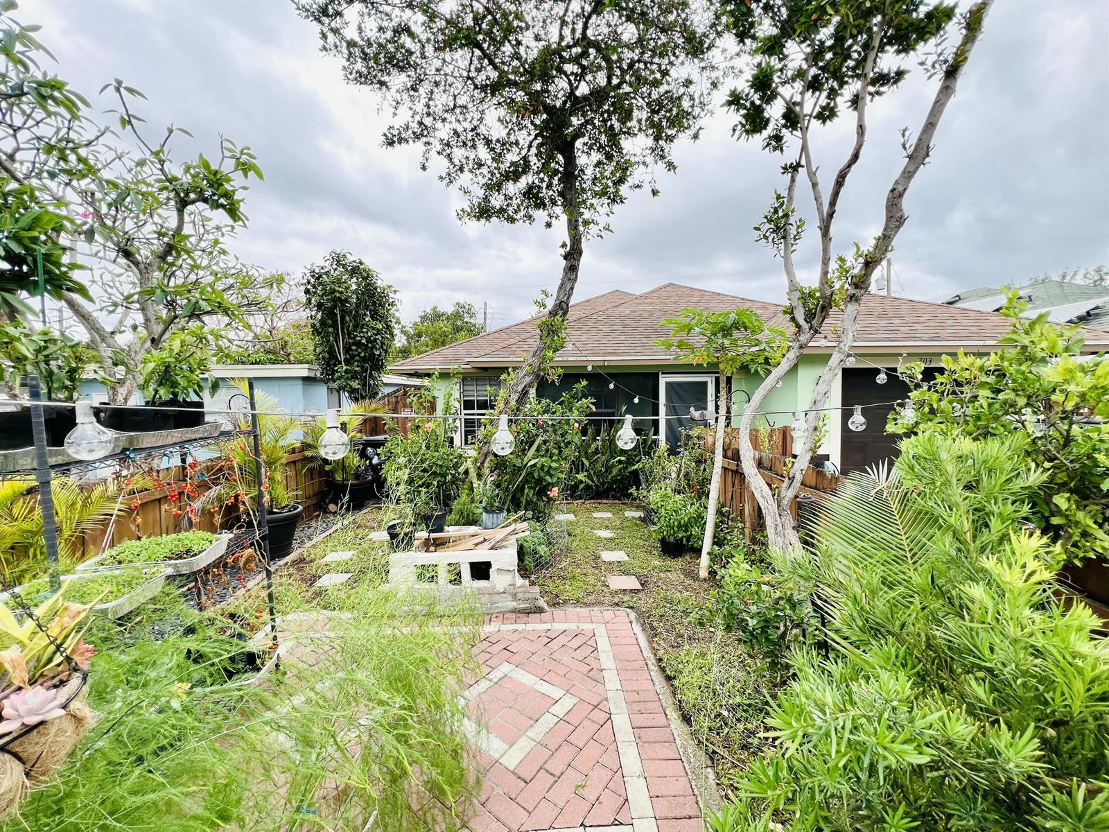 A backyard garden features a brick patio, string lights, and various potted plants and trees — 703 S A Street S, FL 33460, FL