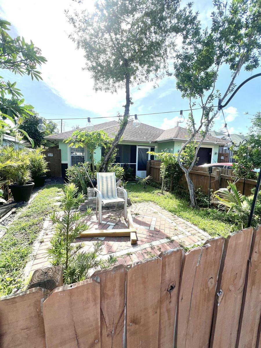 A backyard features a brick patio, a single chair, string lights, and a wooden fence — 703 S A Street S, FL 33460, FL