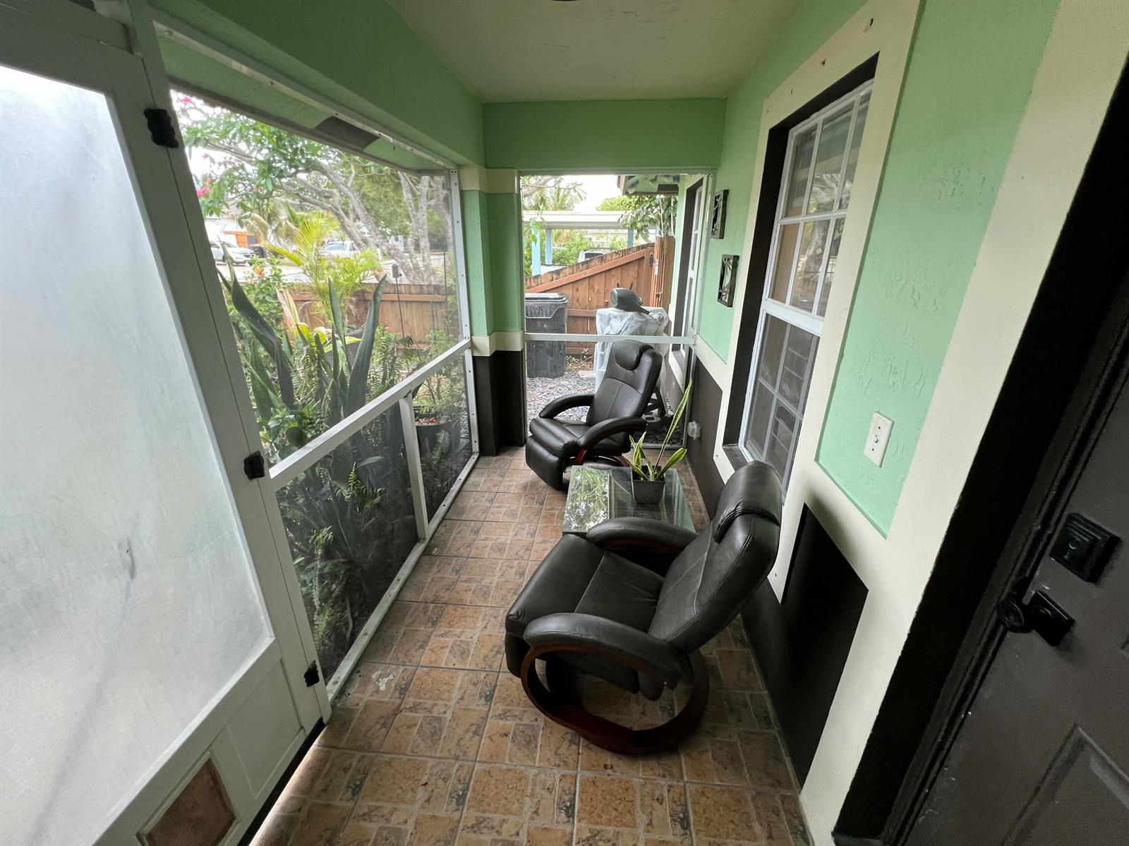 A screened-in porch with tiled flooring, two leather armchairs, and a small glass table — 703 S A Street S, FL 33460, FL