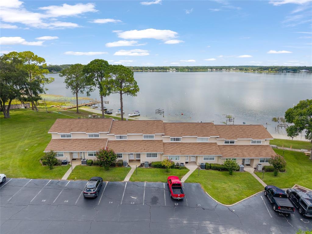 An aerial view shows a multi-unit townhouse building situated next to a large lake — 11001 SE SUNSET HARBOR ROAD UNIT B13, SUMMERFIELD, FL