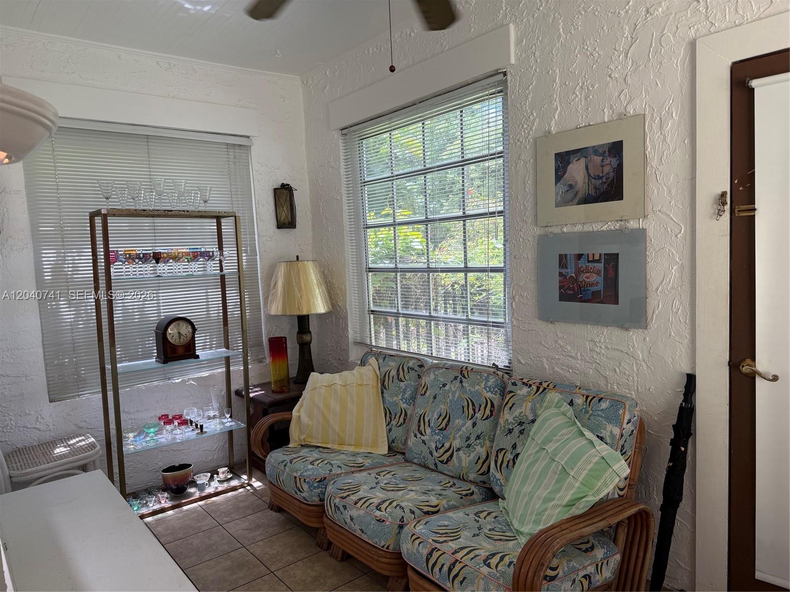 A sunroom features a patterned sofa, a metal display shelf, and textured white walls — 1209 Aguila Ave, Coral Gables FL 33134, CORAL GABLES, FL
