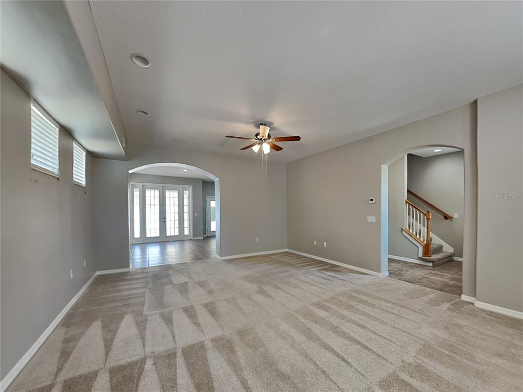 A carpeted living room features a ceiling fan, arched doorways, and a staircase — 33314 PORTAL DRIVE, LEESBURG, FL