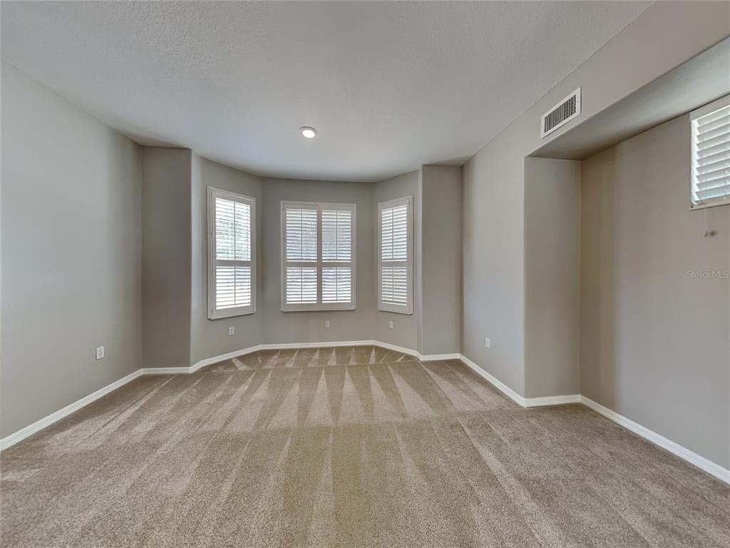 An empty room with beige carpet, light gray walls, and a three-window bay area — 33314 PORTAL DRIVE, LEESBURG, FL
