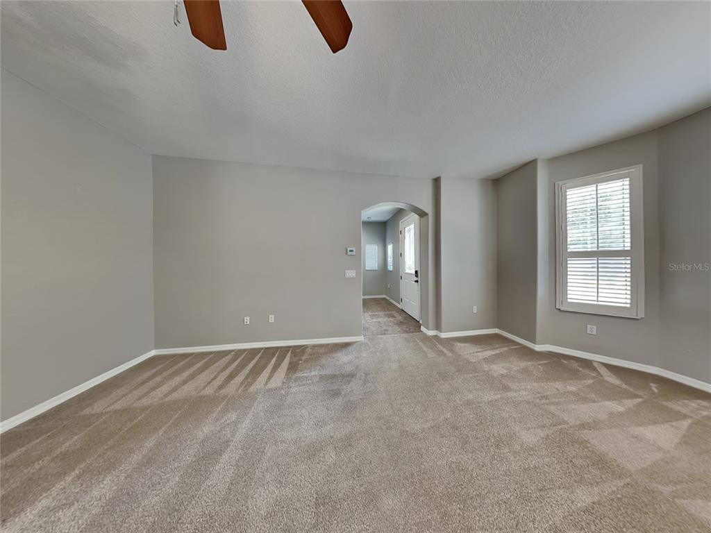 An empty living room features gray walls, beige carpeting, an arched doorway, and a window — 33314 PORTAL DRIVE, LEESBURG, FL