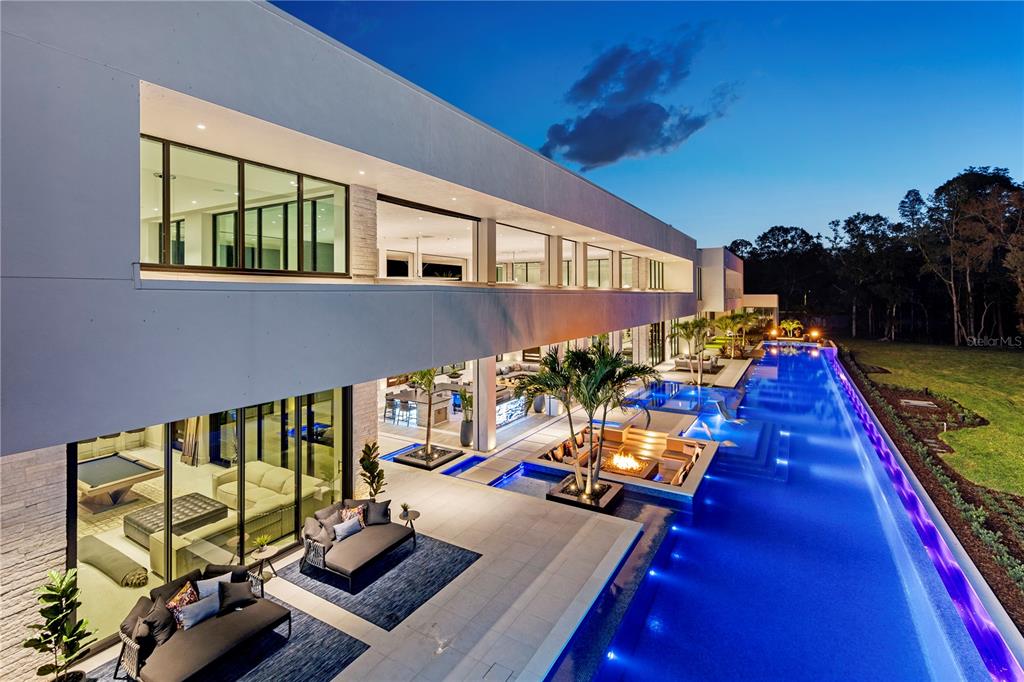 A modern two-story home features a long lap pool, outdoor seating, and a fire pit — 18725 JIRETZ ROAD, ODESSA, FL
