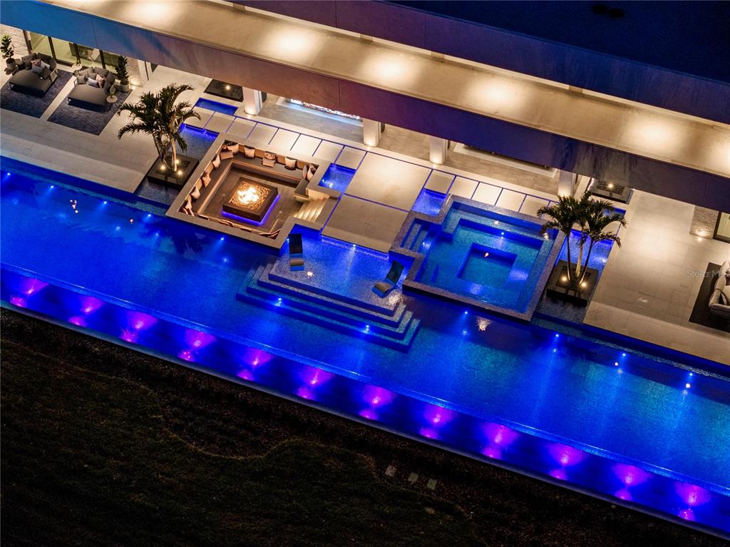 An aerial view of a modern home exterior featuring a long, illuminated swimming pool — 18725 JIRETZ ROAD, ODESSA, FL