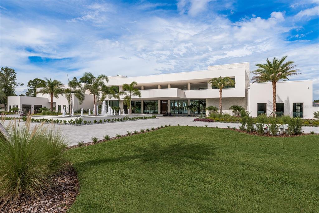 A modern white mansion features a large fountain in front of a paved circular driveway — 18725 JIRETZ ROAD, ODESSA, FL