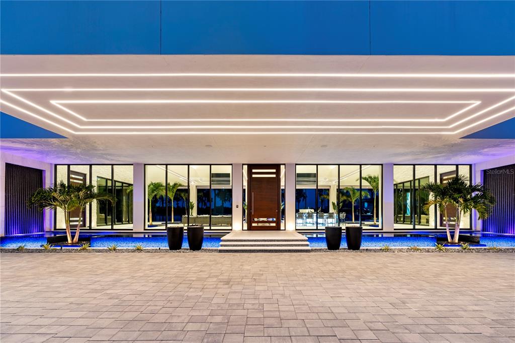 A modern house entrance features a paved driveway, a reflecting pool, and recessed linear lighting — 18725 JIRETZ ROAD, ODESSA, FL