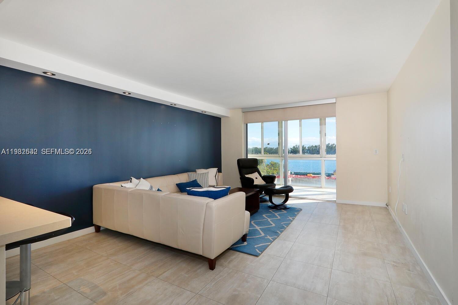 A living room features a dark blue accent wall, beige sofa, and floor-to-ceiling water views — 145 SE 25th Rd # 502, Miami FL 33129, MIAMI, FL