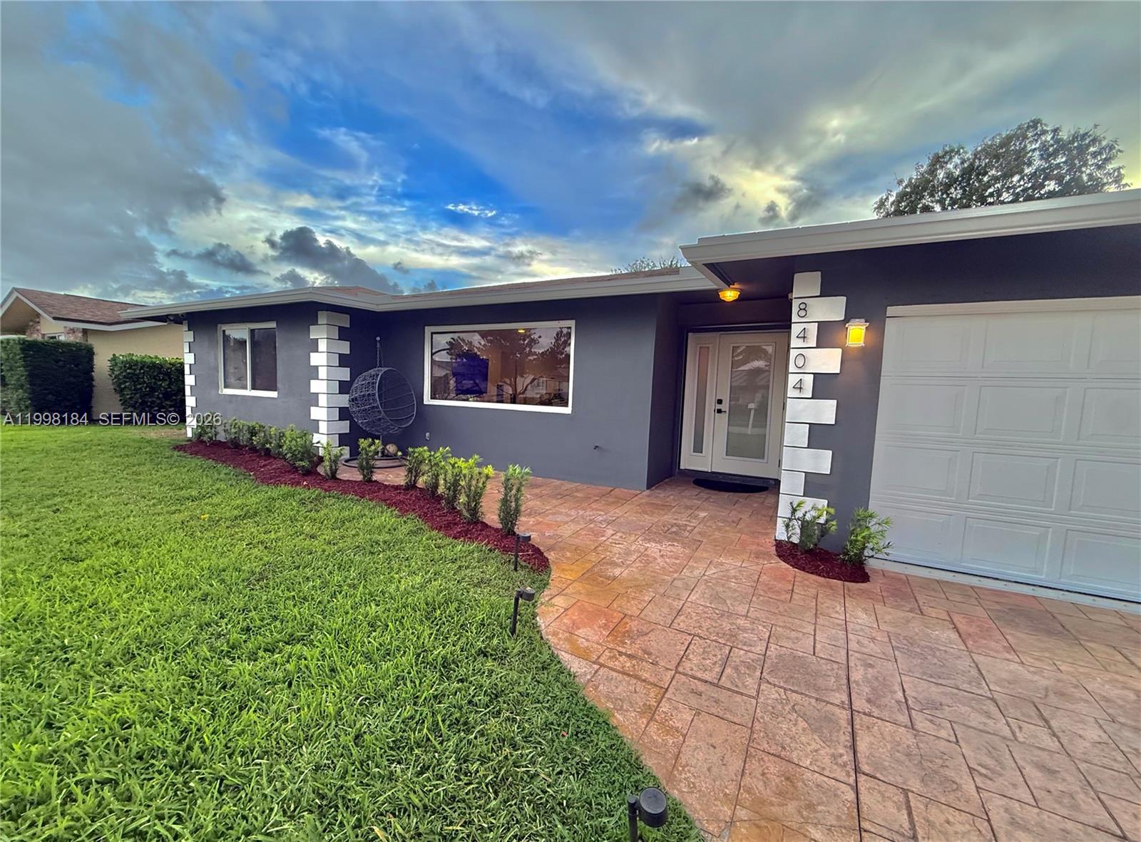 A gray house with a white-trimmed garage and a stone walkway leading to the entrance — 8404 SW 26th St, Davie FL 33324, DAVIE, FL