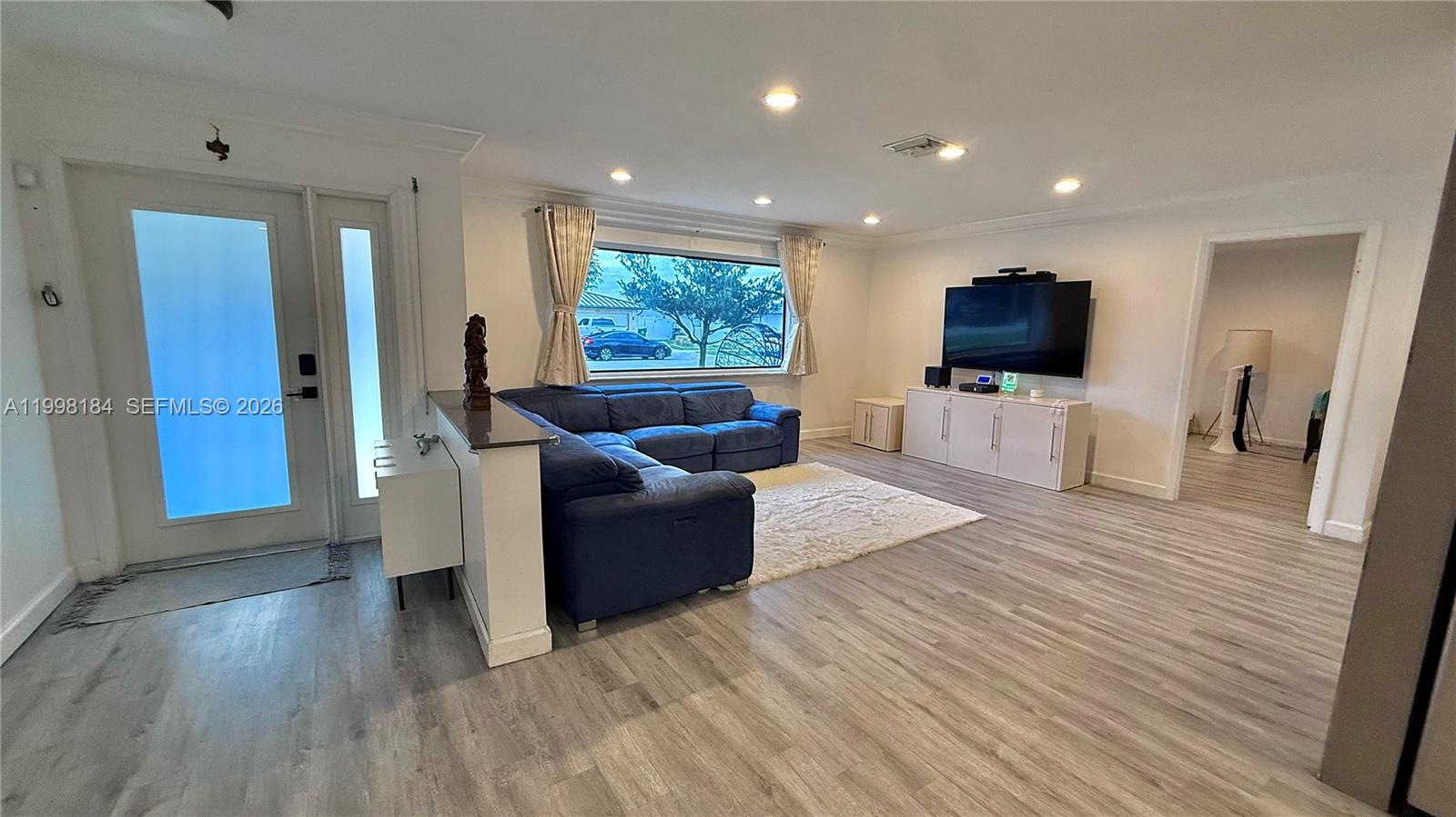 A living room features a blue sectional sofa, a wall-mounted television, and light wood flooring — 8404 SW 26th St, Davie FL 33324, DAVIE, FL
