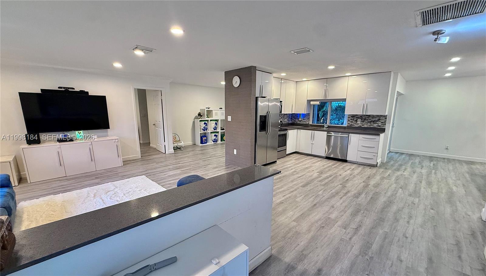 An open-concept kitchen and living area feature gray wood-look flooring and white cabinetry — 8404 SW 26th St, Davie FL 33324, DAVIE, FL