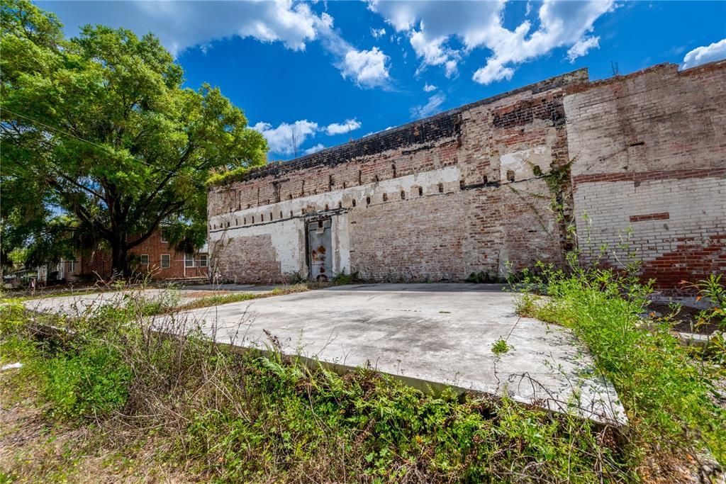 An exterior view of a weathered brick building wall with a single door and concrete slab — 98 NW 254TH STREET, NEWBERRY, FL