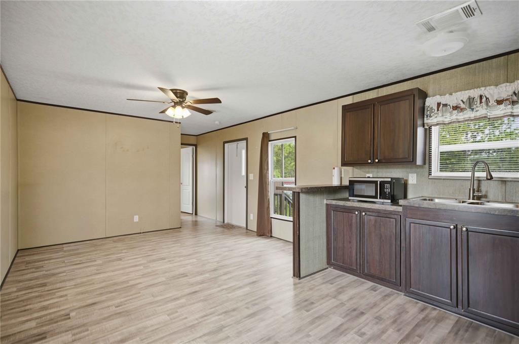 A kitchen and living area with dark cabinets, black appliances, and light wood-look flooring — 3342 SW 166TH COURT ROAD, OCALA, FL