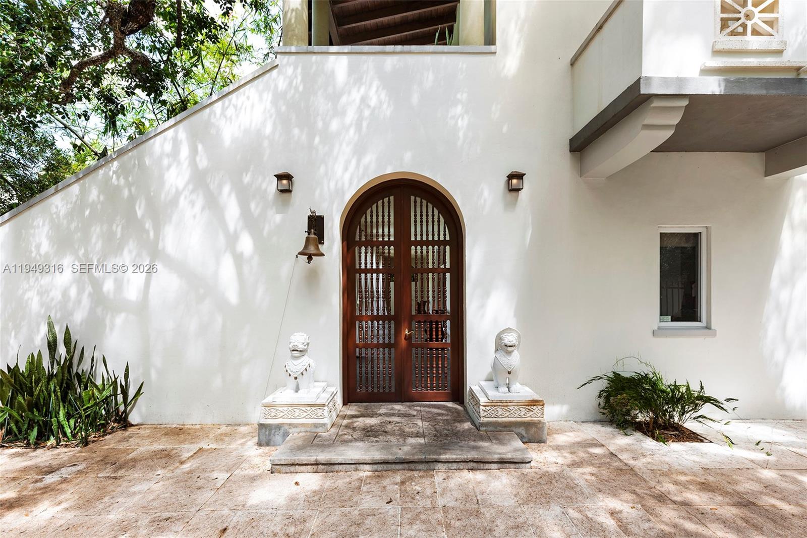 An arched wooden door with spindle details is flanked by two stone lion statues — 4191 Lybyer Ave, Miami FL 33133, MIAMI, FL