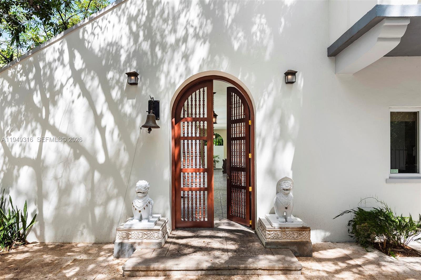An arched wooden door with spindle details is flanked by two stone lion statues — 4191 Lybyer Ave, Miami FL 33133, MIAMI, FL