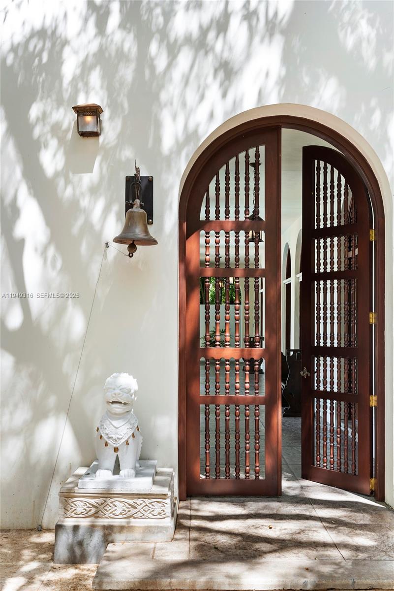 An arched wooden door with spindle details stands beside a stone lion statue and bell — 4191 Lybyer Ave, Miami FL 33133, MIAMI, FL