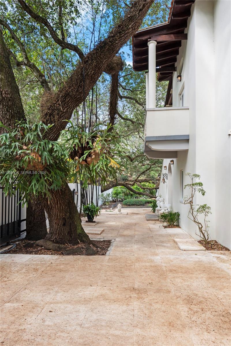 A paved outdoor walkway runs alongside a white building beneath a large, mature tree — 4191 Lybyer Ave, Miami FL 33133, MIAMI, FL