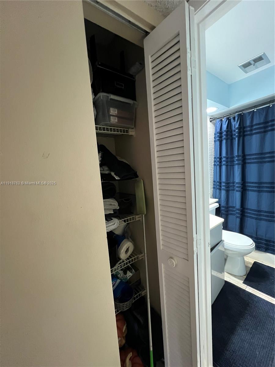 A narrow linen closet with wire shelving stands next to a bathroom with a shower — 4900 SW 149th Ct # 12C, Miami FL 33185, MIAMI, FL