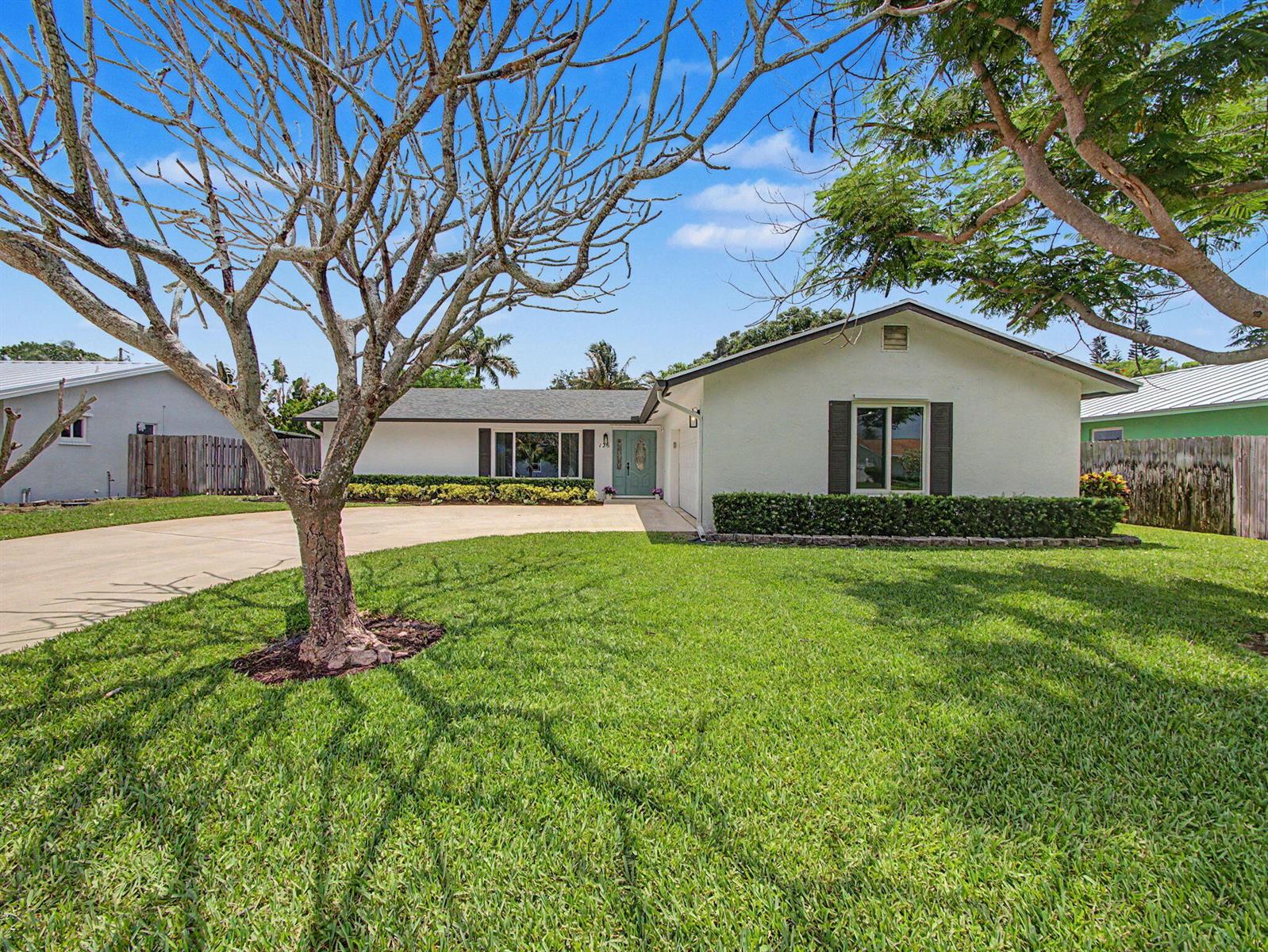 A single-story white house with a green door, a large lawn, and mature trees — 126 Chapel Lane, Tequesta FL 33469, TEQUESTA, FL