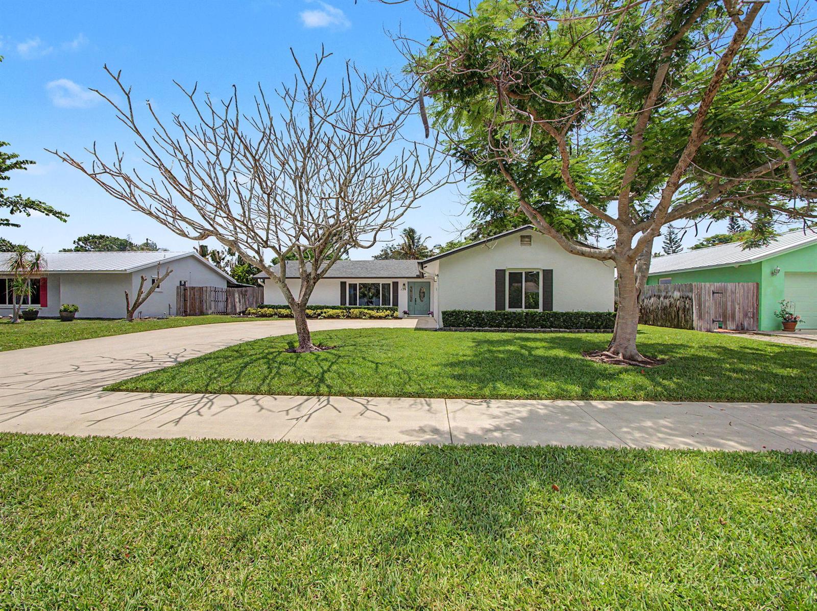 A single-story house with a light-colored exterior, a large front lawn, and two trees — 126 Chapel Lane, Tequesta FL 33469, TEQUESTA, FL