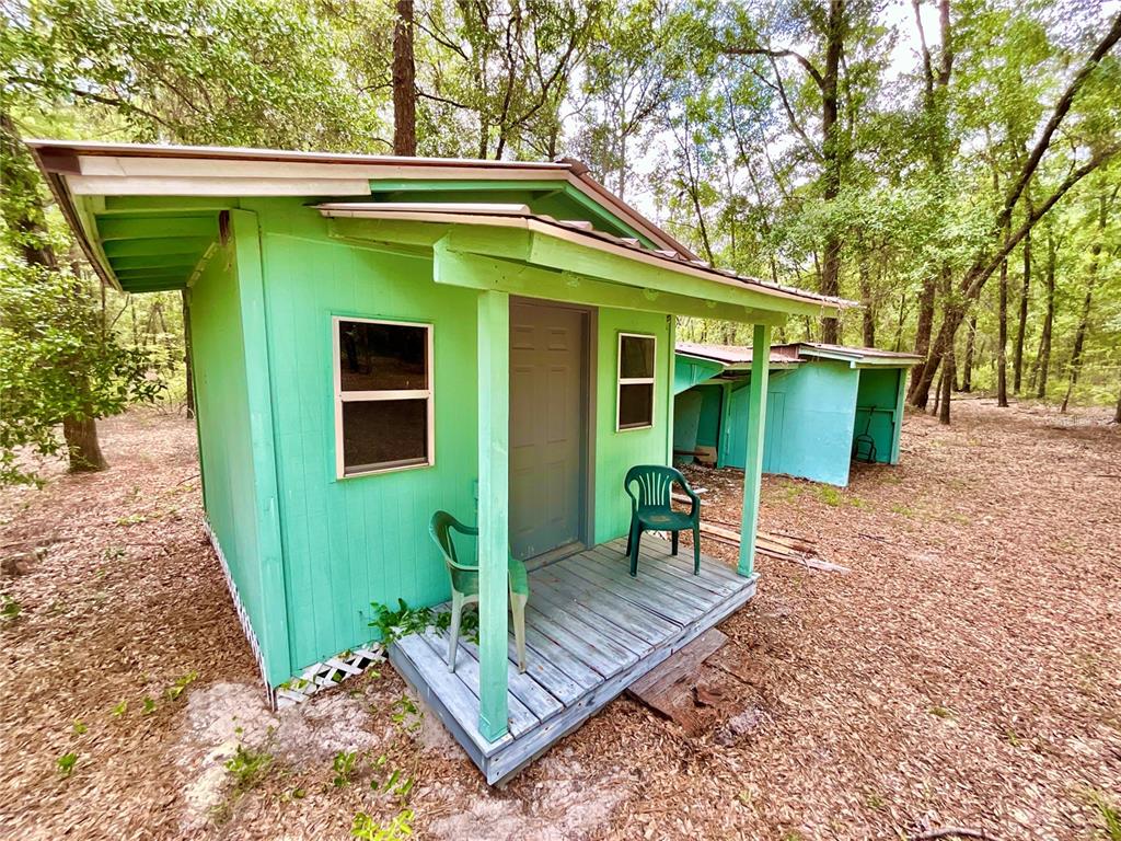 A small, bright green wooden cabin with a front porch sits in a wooded area — 8232 SWAN LAKE ROAD, MELROSE, FL