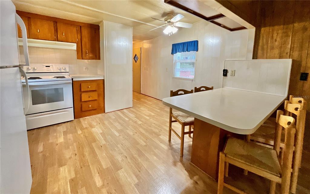 A kitchen features wood cabinets, a white stove, a breakfast bar, and light wood flooring — 8232 SWAN LAKE ROAD, MELROSE, FL