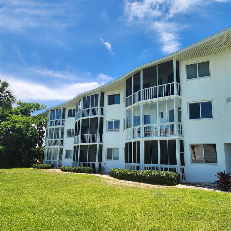 An aerial view shows a multi-story apartment building situated on a waterfront peninsula near a bridge — 777 JOHN RINGLING BOULEVARD UNIT 24, SARASOTA, FL