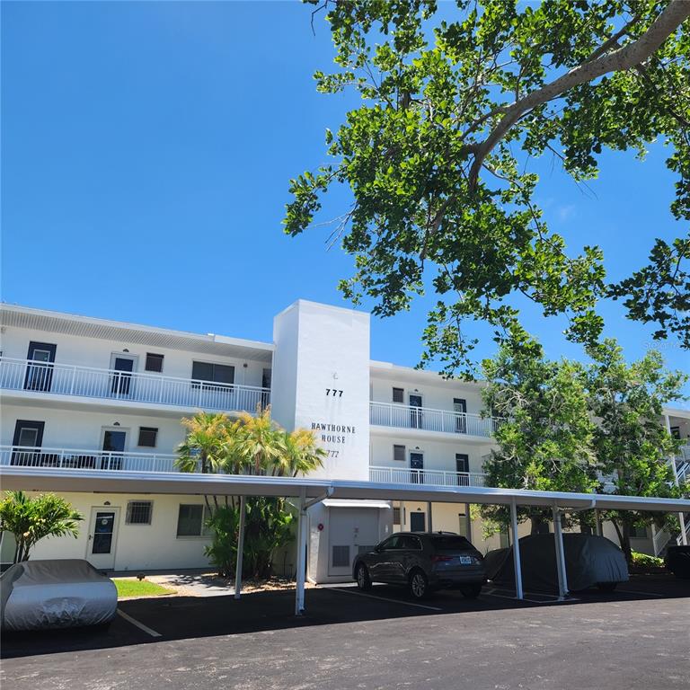 A multi-story white apartment building sits behind a large, manicured green lawn — 777 JOHN RINGLING BOULEVARD UNIT 24, SARASOTA, FL