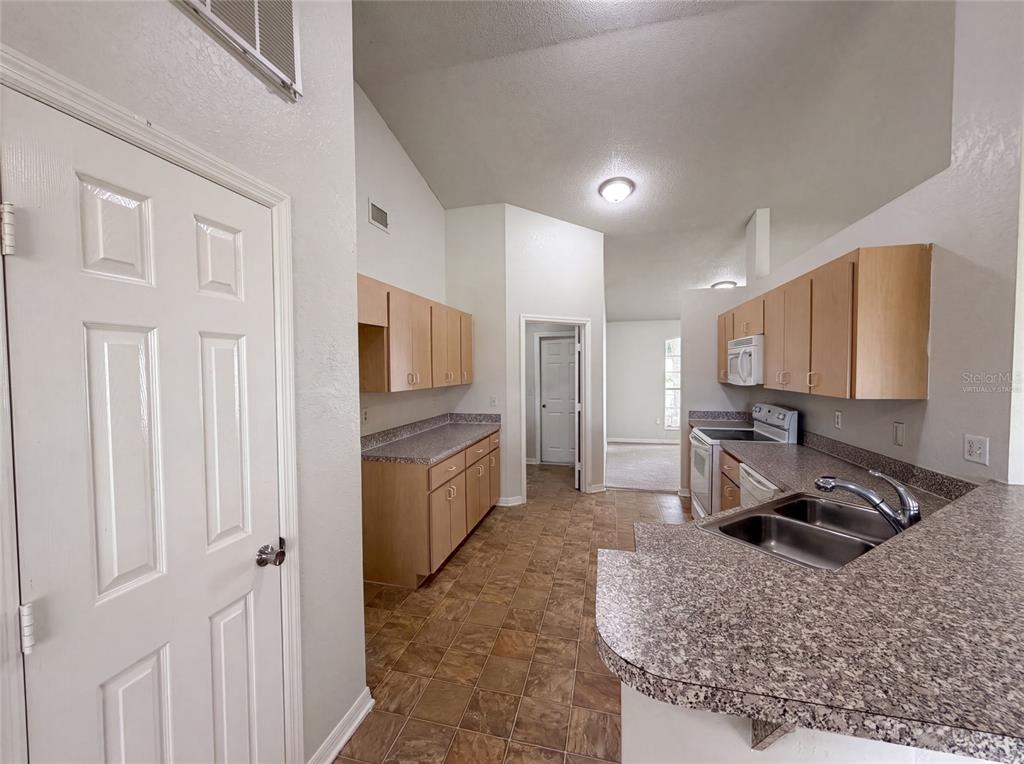 A kitchen features light wood cabinets, speckled laminate countertops, and tile flooring under a vaulted ceiling — 1038 HIGHLAND CREST CIRCLE, LAKE WALES, FL