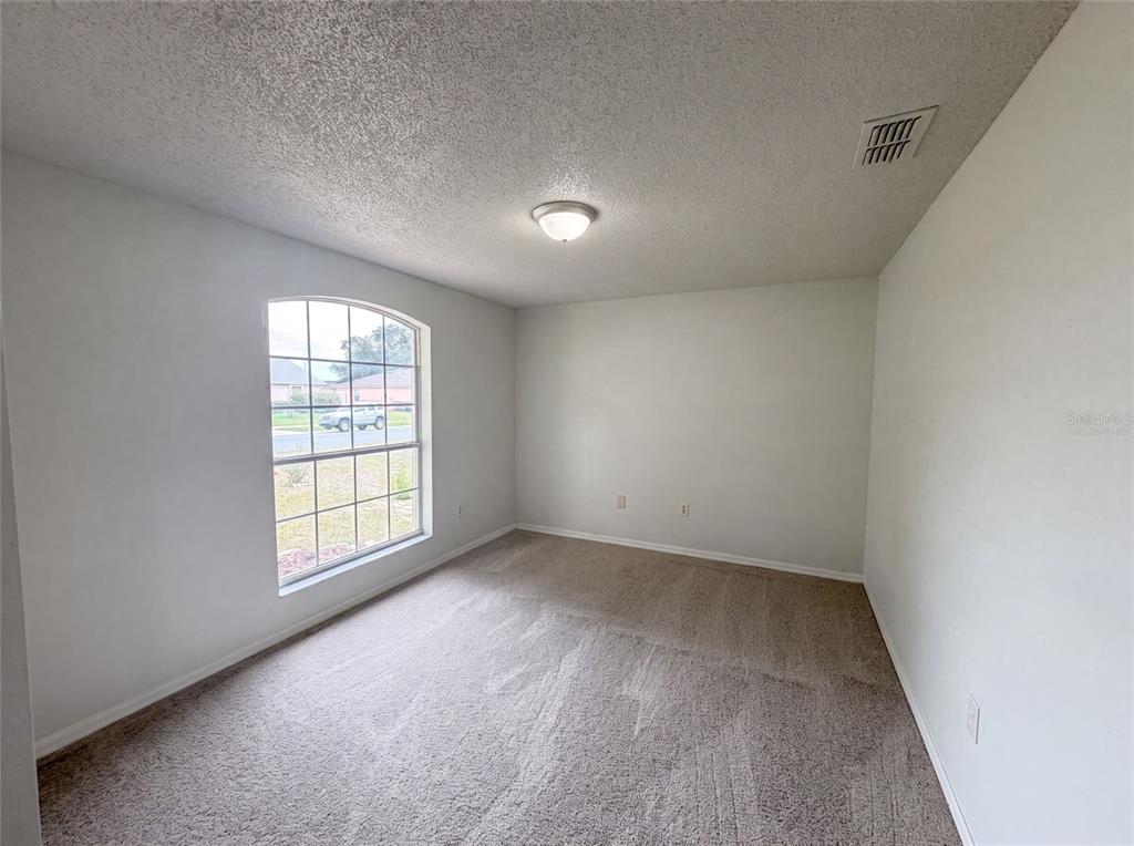 An empty bedroom features beige carpet, white walls, a ceiling light, and an arched window — 1038 HIGHLAND CREST CIRCLE, LAKE WALES, FL