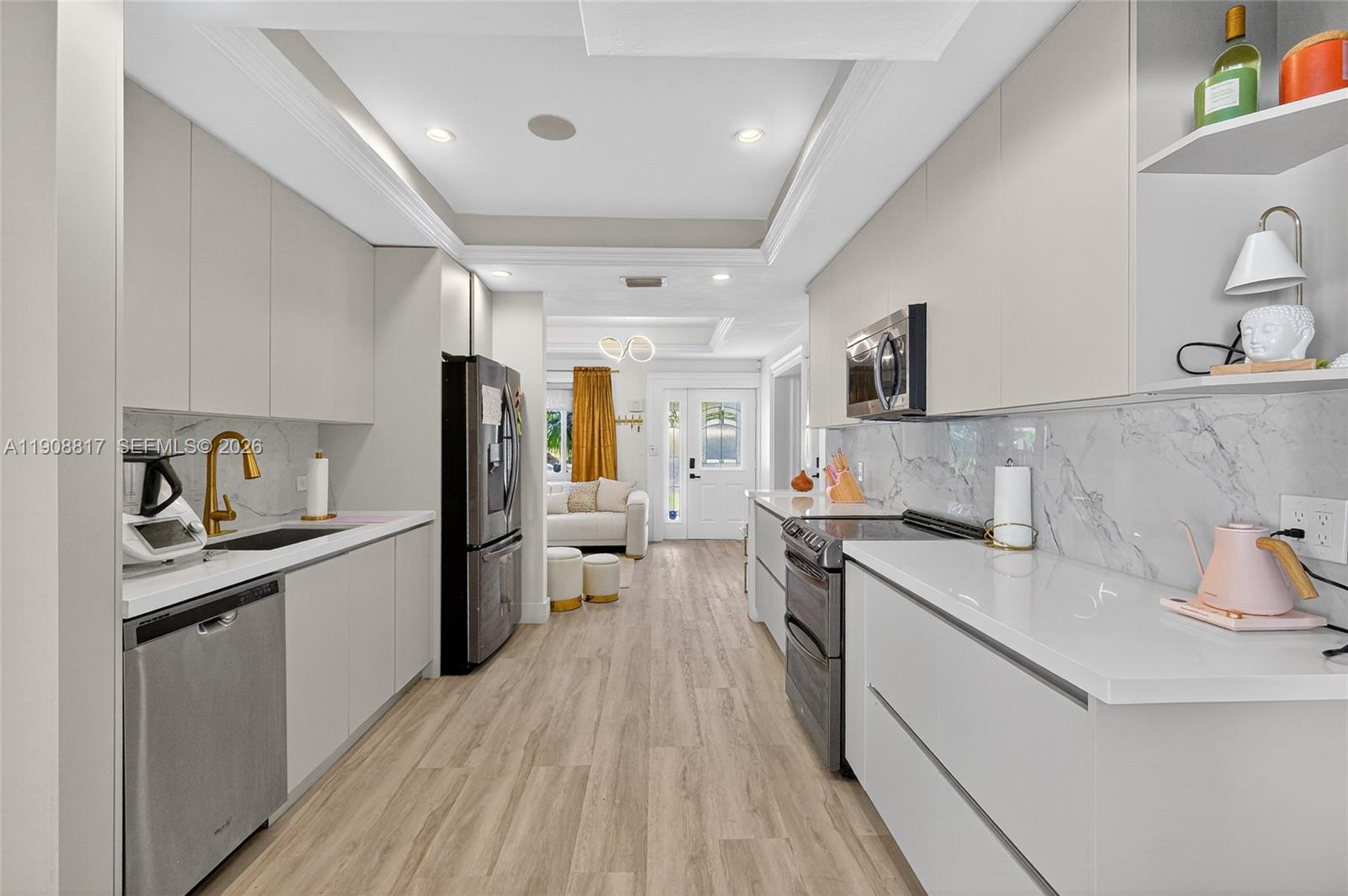 A modern galley kitchen features light gray cabinetry, white countertops, and stainless steel appliances — 155 NW 124th St, North Miami FL 33168, NORTH MIAMI, FL