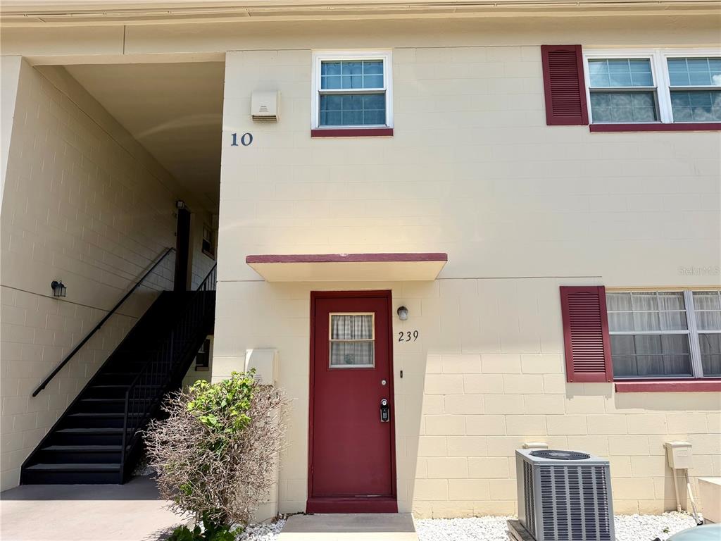 A two-story building exterior features a red front door, a staircase, and a window — 5505 HERNANDES DRIVE UNIT 239, ORLANDO, FL
