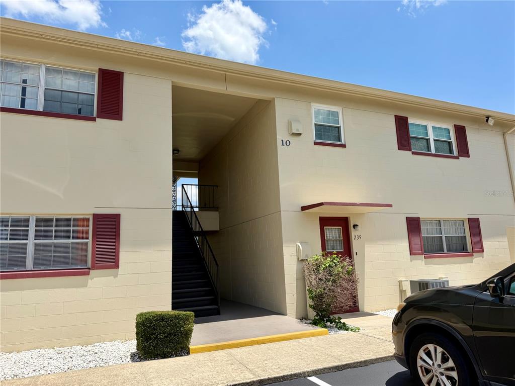 A two-story apartment building exterior features tan block walls, red shutters, and an outdoor staircase — 5505 HERNANDES DRIVE UNIT 239, ORLANDO, FL