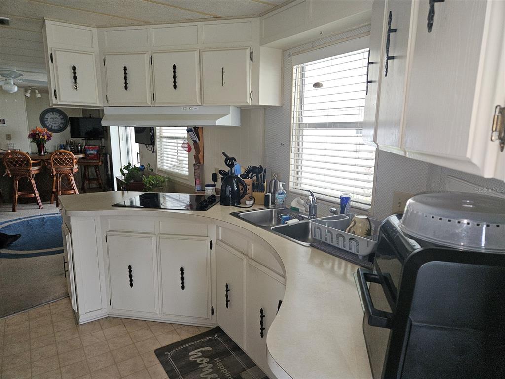A kitchen features white cabinets, a double sink, a stovetop, and a curved countertop — 26087 COUNTESS LANE, BONITA SPRINGS, FL