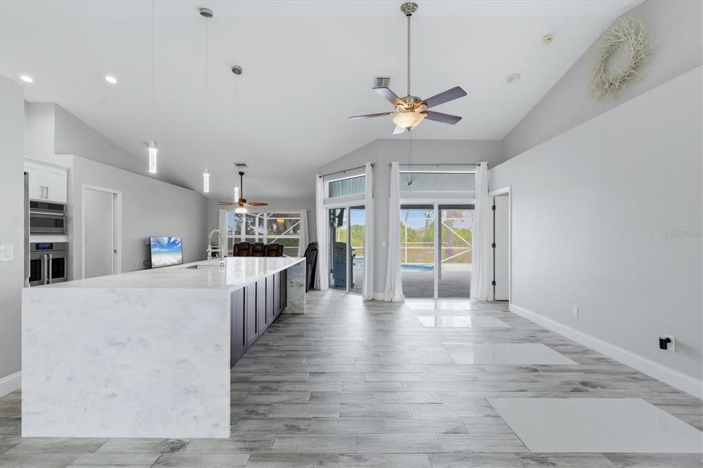 A modern kitchen with a large marble island overlooks a living area and pool patio — 8188 WELSFORD ROAD, PORT CHARLOTTE, FL